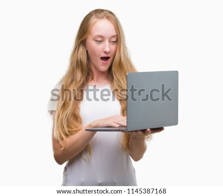 Blonde teenager woman using computer laptop scared in shock with a surprise face, afraid and excited with fear expression