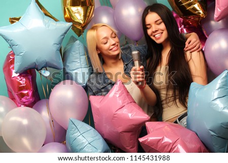 holidays, friends   and people concept -  two women in casual wear with microphone singing karaoke over  background of colorful ballons