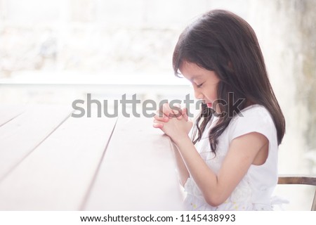 Little girl praying in the morning on the wooden table.Little asian girl hand praying, Kid praying to God,Hands folded in prayer concept for Christianity, faith, spirituality and religion.