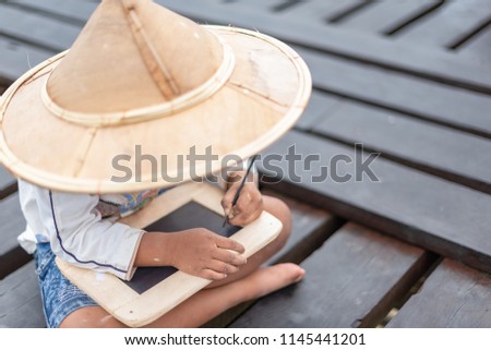 Little boy in Asian country pay attention on his writing. Child happy to learn. Happy boys getting a blackboard writing his name. Pre-school boy shows his hand writing outdoor.