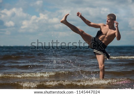 Kickboxer kicks in the open air in summer against the sea. Combat sport