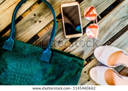 Top view green big casual bag with snake print, round glasses, golden phone and pair of female high-heeled shoes on a wooden background. Modern fashion concept and everyday women's clothing and acce Royalty-Free Stock Photo #1145460662