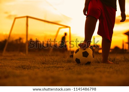 Close up picture of an old ball and foot of a poor kid who is playing football in the sunshine day.