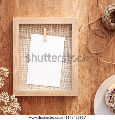 Frame mockup, white donut with colorful cupcakes, a string and white flowers in a vase on a wooden table