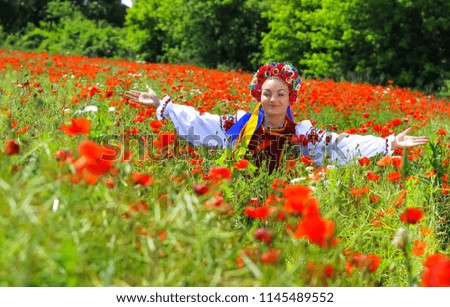 young beautiful woman with blond long hair in national dress red skirt and a white shirt with a wreath of flowers in a field of poppies and wheat