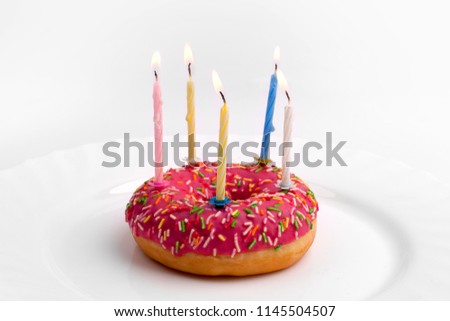 Donut in the form of a birthday cake with burning candles on a white plate on a white background close up