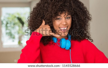 African american woman wearing headphones smiling doing phone gesture with hand and fingers like talking on the telephone. Communicating concepts.