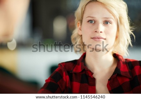 Head and shoulders portrait of creative  young woman wearing casual shirt listening to colleague during meeting and smiling, copy space