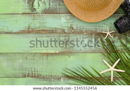 Freelance concept summer hat, camera, seastars and paln leaf on green wooden background Top View Close-up flat lay