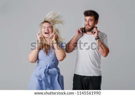 Young cheerful couple listening to loud music in wireless headphones. The girl waving long hair and dancing, the guy looks at her in surprise
