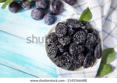 Prunes in a bowl on an old wooden table on a background of fresh plums. Prunes and fresh plums on the table top view.