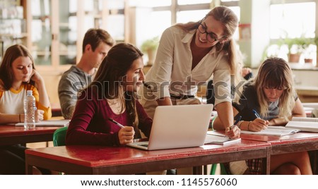 Smiling female lecturer helping student during her class. Student in a lecture with helpful teacher. Royalty-Free Stock Photo #1145576060