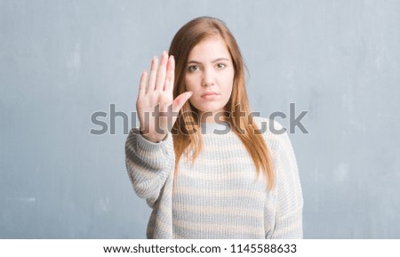Young adult woman over grey grunge wall with open hand doing stop sign with serious and confident expression, defense gesture