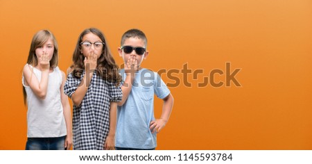 Group of boy and girls kids over orange background cover mouth with hand shocked with shame for mistake, expression of fear, scared in silence, secret concept