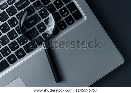 Laptop computer with magnifying glass on dark background, concept of search. Internet security conceptual image. Top view. Flat lay. Close up