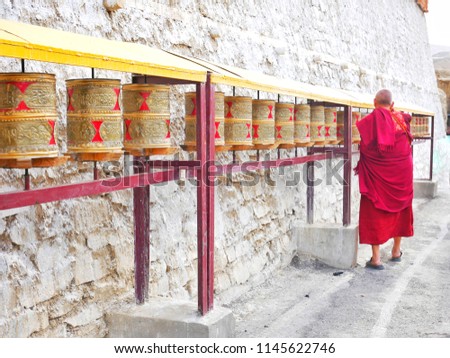 The texture of beautiful antique Tibetan style prayer wheels near stone brick wall with the Tibetan monk.