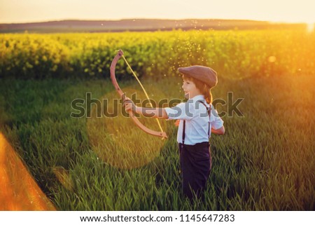 Portrait of child playing with bow and arrows, archery shoots a bow at the target on sunset Royalty-Free Stock Photo #1145647283