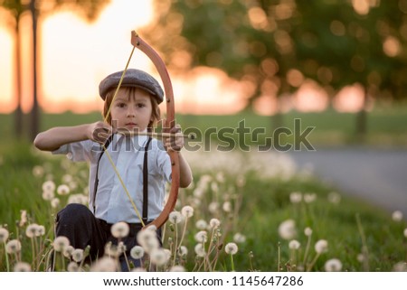 Portrait of child playing with bow and arrows, archery shoots a bow at the target on sunset Royalty-Free Stock Photo #1145647286