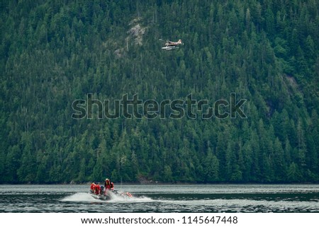 Group of people exploring an Alaskan fjord in a zodiac with a seaplane flying over them
