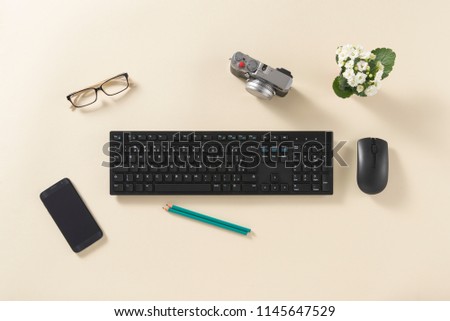 Top view of desk with camera, smartphone, flowers, keyboard, mouse, glasses and pencil, on a clean background