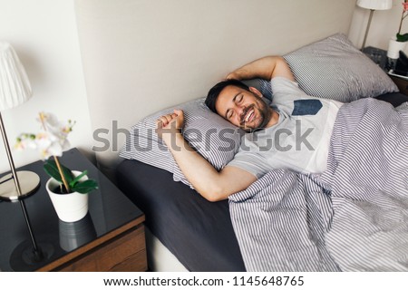 Young man sleeping waking up and stretching in his bed Royalty-Free Stock Photo #1145648765