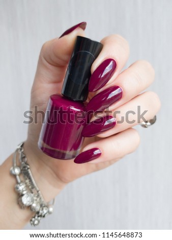 Female hand with long nails and bottle with bordo nail varnish
