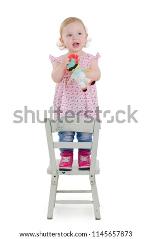 Beautiful baby girl holding doll, is standing on a old wooden white chair, looking up, Isolated on white background