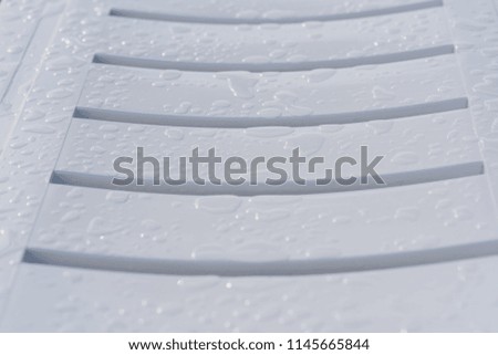 Fragment of wet white plastic deck chair close up