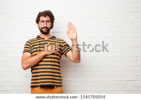 young dumb man smiling confidently while making a sincere promise or oath, solemnly swearing with one hand over heart.