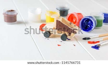 Multi-colored brushes and jars of paint on a white wooden table.