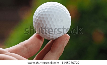 Close up golf ball on woman hand with green plants background. Golf sport ideas and background. 