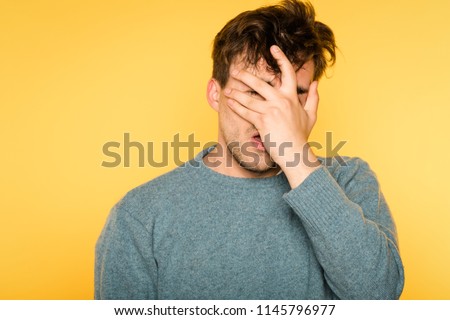 facepalm. desperate frustrated man covering his face. hopeless situation and regret or hangover. portrait of a young brunet guy on yellow background. emotion facial expression and feelings concept. Royalty-Free Stock Photo #1145796977