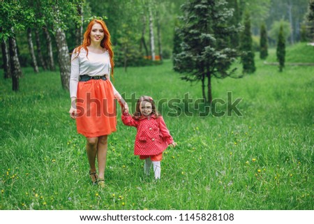 beautiful young red-haired mother with little daughter walking in the green park