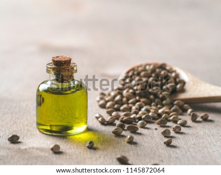 Hemp seeds and hemp oil on brown wooden table. Hemp seeds in wooden spoon and hemp essential oil in small glass bottle. Copy space for text Royalty-Free Stock Photo #1145872064