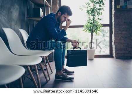 Attractive handsome young brunet bearded executive worker serious man in office work station work place, sitting, tired of waiting for job interview. Carrying brief-case