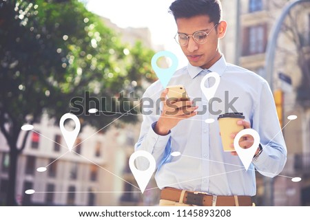 Serious student sending messages to friends in social network. Young male searching via app food restaurants near his location. Maps application for smartphone. Infographics tags with virtual map Royalty-Free Stock Photo #1145893208