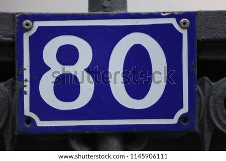 Close up outdoor view of the number eighty written in white on a blue rectangular metallic plate. Sign 80 to indicate the address of a house in France. Isolated numerical element place on a gate. 