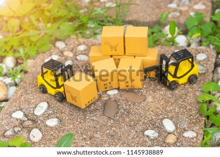 Mini forklift truck load cardboard box with shopping cart symbol on stone block with grass pavement. Logistics and transportation management ideas and Industry business commercial concept.