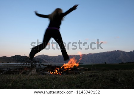 A woman jumping over a campfire