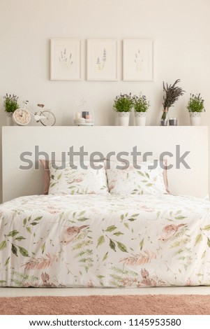 Real photo of floral bedroom interior with a double bed, pillows, plants and paintings