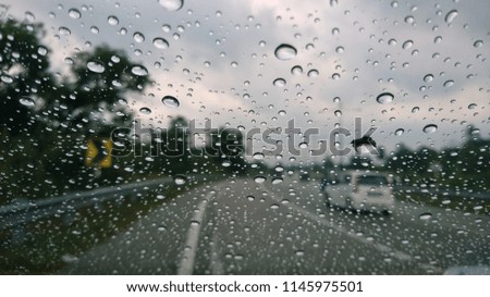 The rain drops on the windshield of the car. Selective focus on the curved road.