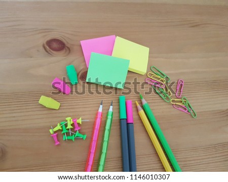 Small notepads with colored pencils, markers, paper clips and erasers laying on a wooden desk, School supplies, Office supplies, Writing and drawing utensils