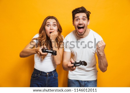 Image of happy man and disappointed woman playing together video games with joysticks isolated over yellow background