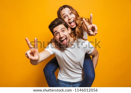 Image of caucasian man having fun and giving piggyback ride to joyful woman isolated over yellow background Royalty-Free Stock Photo #1146012056