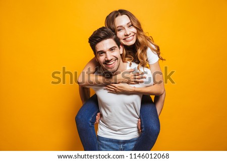 Image of lovely couple having fun while man piggybacking his girlfriend isolated over yellow background