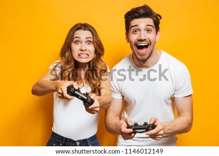 Image of joyful man and displeased woman playing together video games with joysticks isolated over yellow background