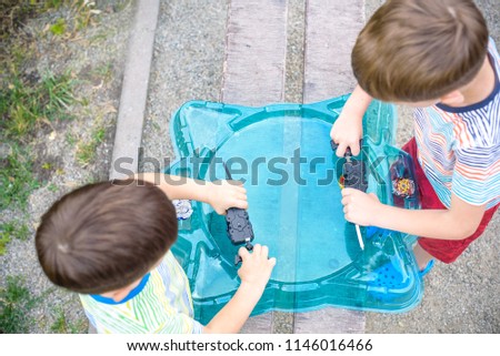 Two Boys playing with modern spin top outdoors. Entertainment game for children. Top, triggered by a trigger. Kids having a tournament on arena or battle field. Top view.