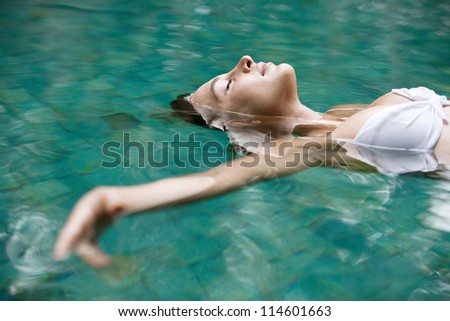 Close up view of an attractive young woman floating on a spa's swimming pool, smiling.