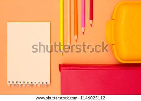 Notebook, book, color pencils and lunch box on pink background
