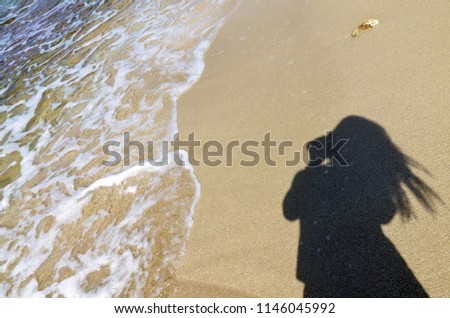 Shadow of a woman taking a photo on the beach on a sunny day